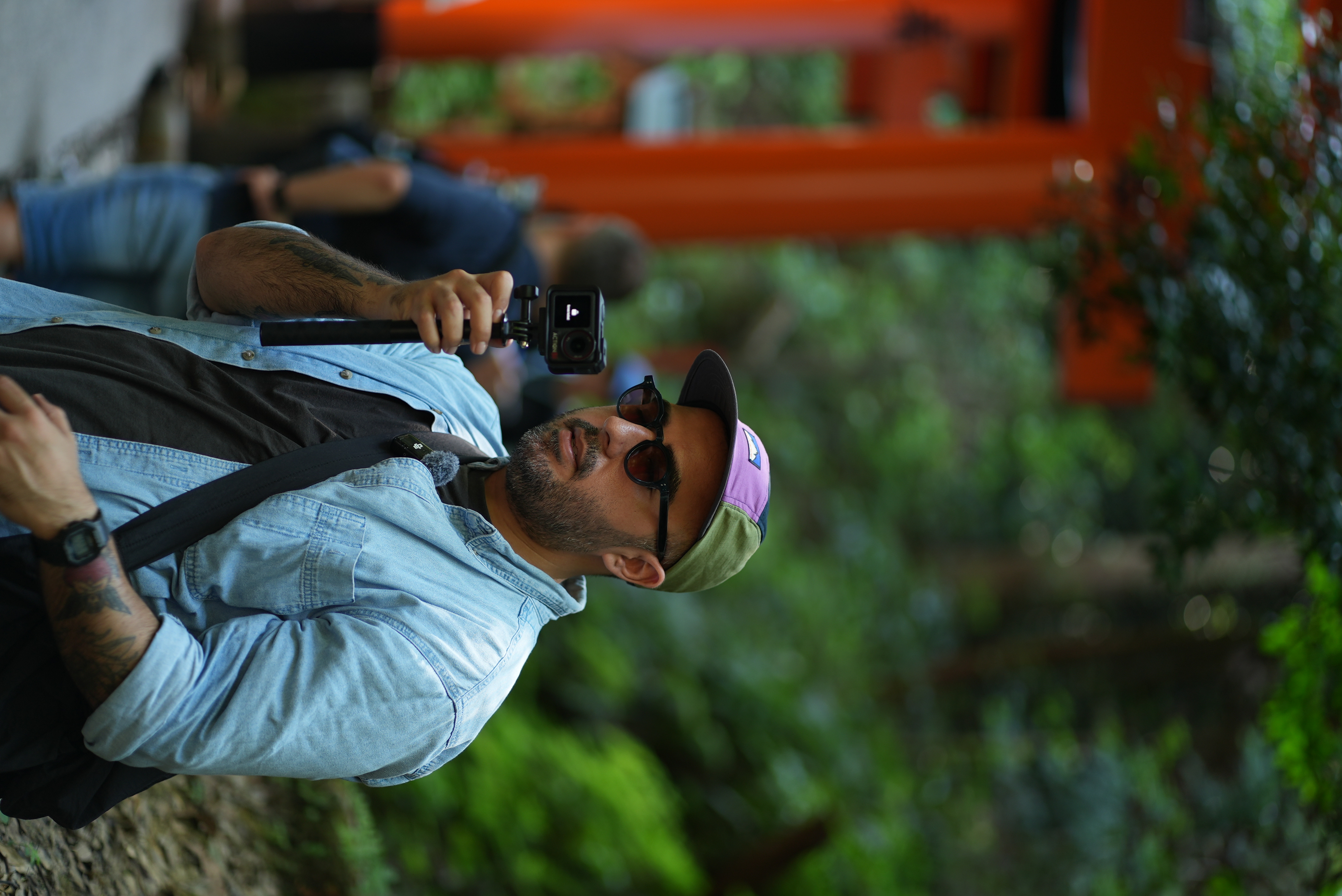Person holding action camera in front of orange torii gates and green foliage